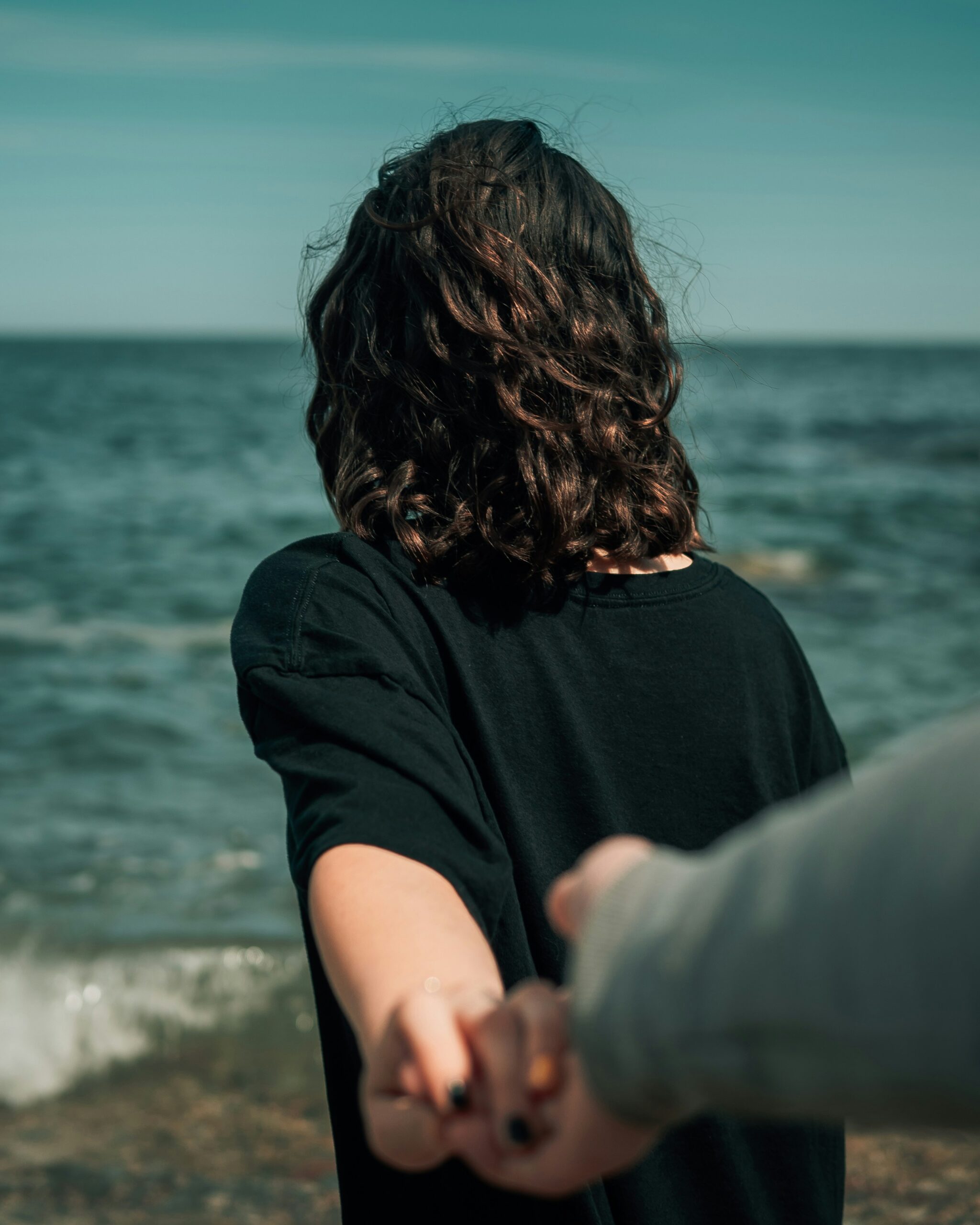 A couple stands on the beach, holding hands with one partner looking away, representing neurodiversity and relationships.