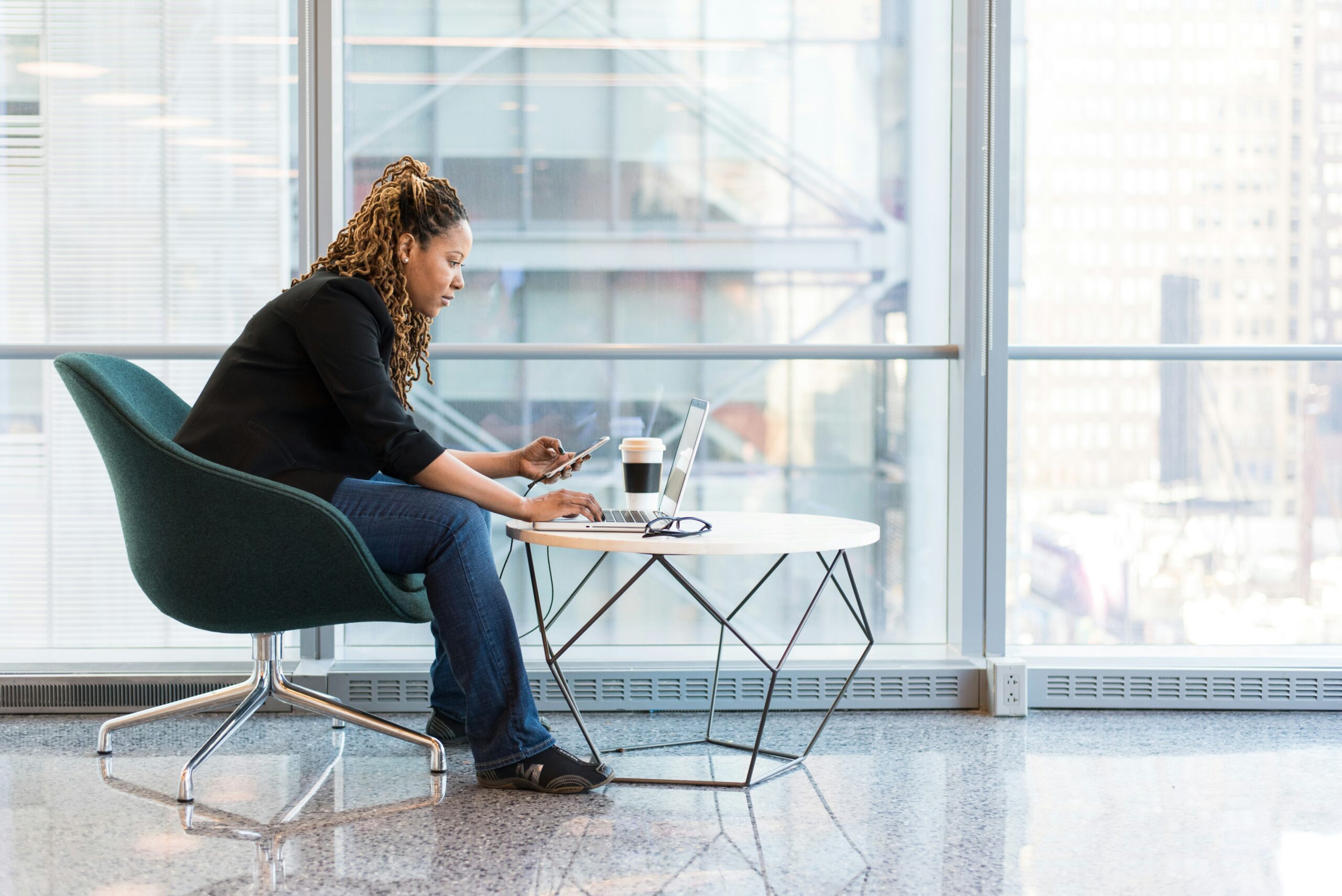 A woman sits at a small table with a cup of coffee and her laptop, completing a consultation for neurodiversity-affirming therapy.
