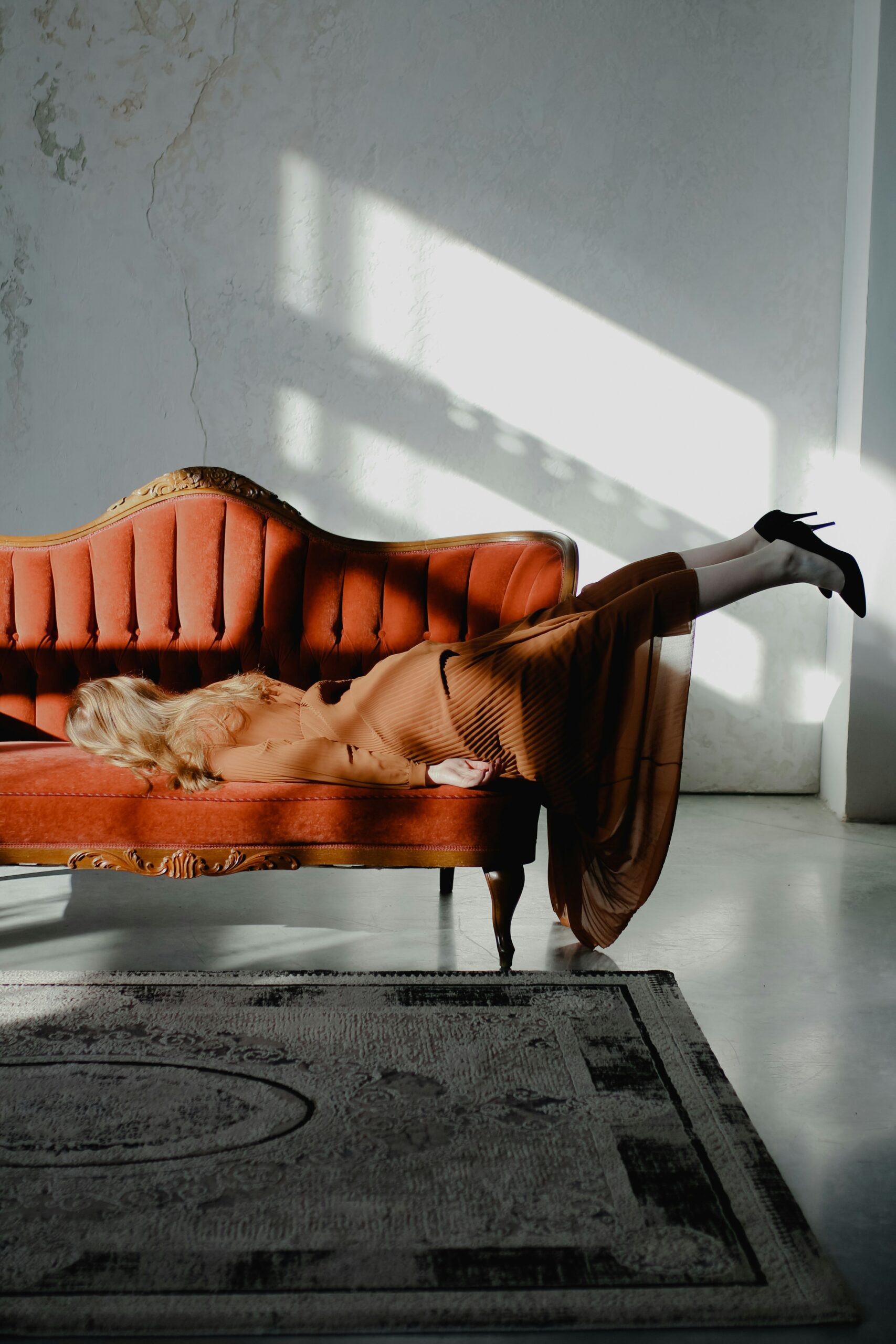 A person lies face down on a orange couch with her feet hanging over the arm rest, symbolizing burnout in ADHD adults.