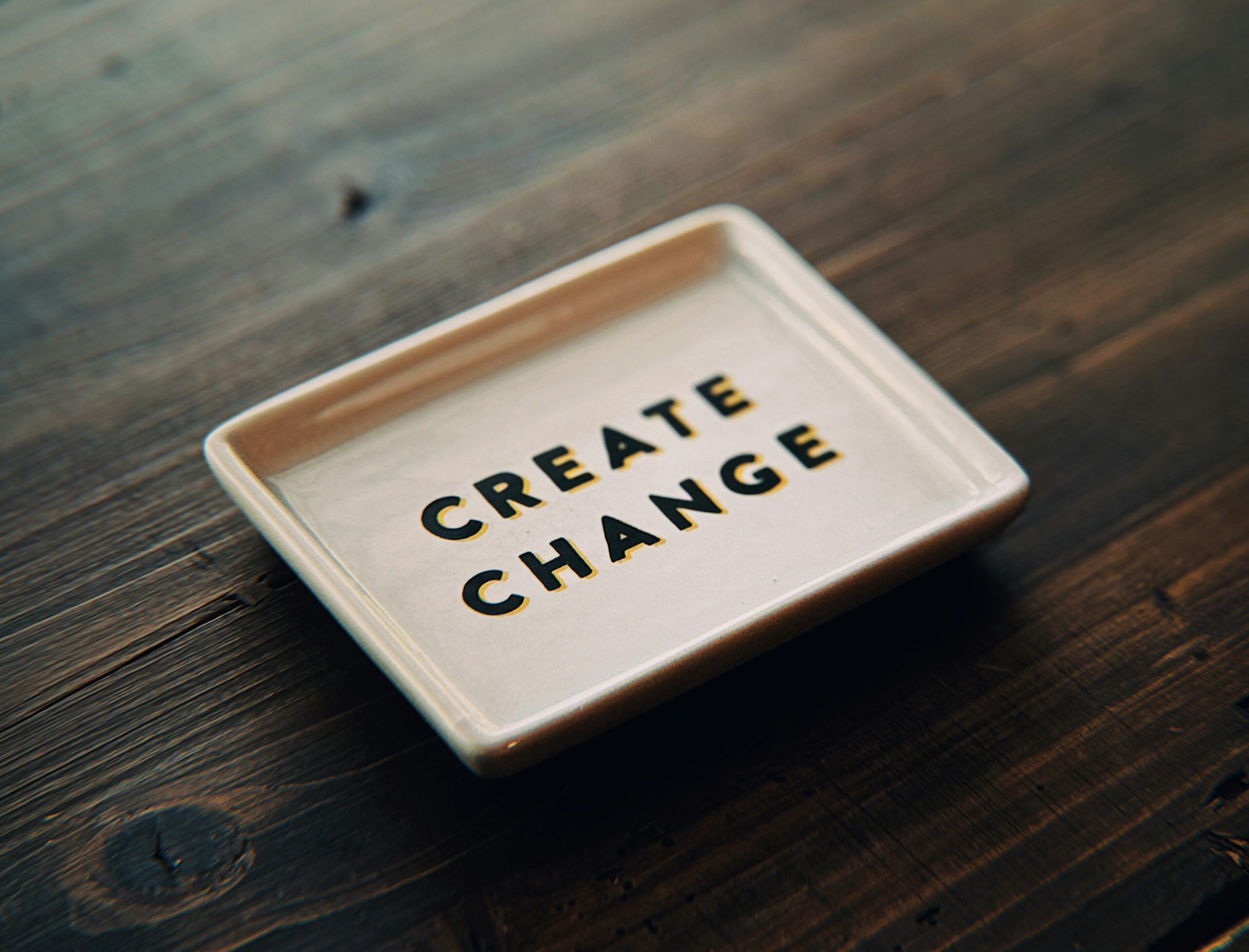 A small white tray on a dark wooden table reads 'create change', representing NeuroSpark Health's mission to change ADHD and autism testing for adults.