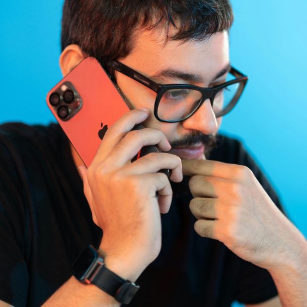 Man with black glasses and a black shirt talking on the phone with a pensive expression thinking about an adult ADHD assessment.