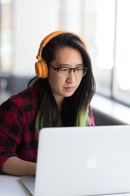 A woman with orange headphones focuses on her computer, representing neurodiversity at work.
