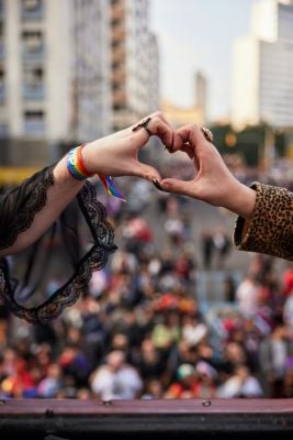 Two people at a Pride event form a heart shape with their hands, celebrating love and unity, symbolizing neuroqueer-resources.