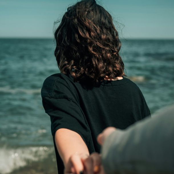 A couple stands on the beach, holding hands with one partner looking away, representing neurodiversity and relationships.