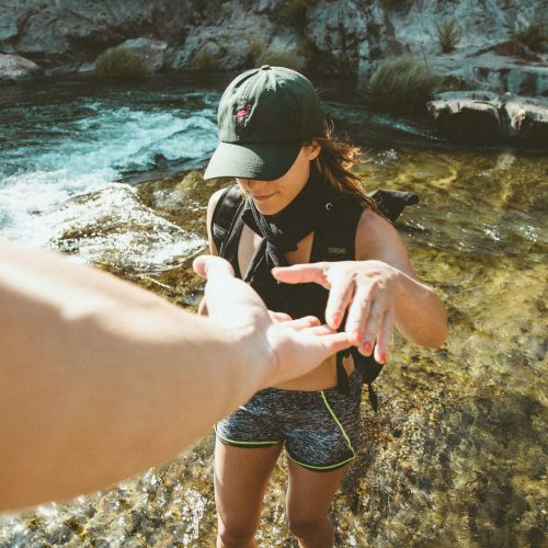 Hand reaching out to support a woman walking in shallow water, representing neurodivergent support services for adults.