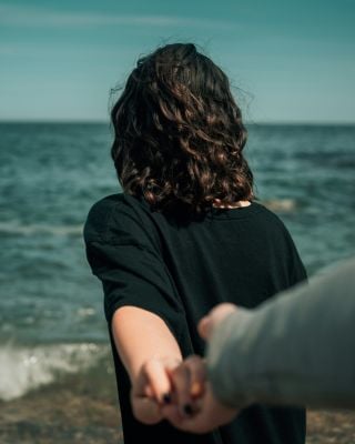 A couple stands on the beach, holding hands with one partner looking away, representing neurodiversity and relationships.