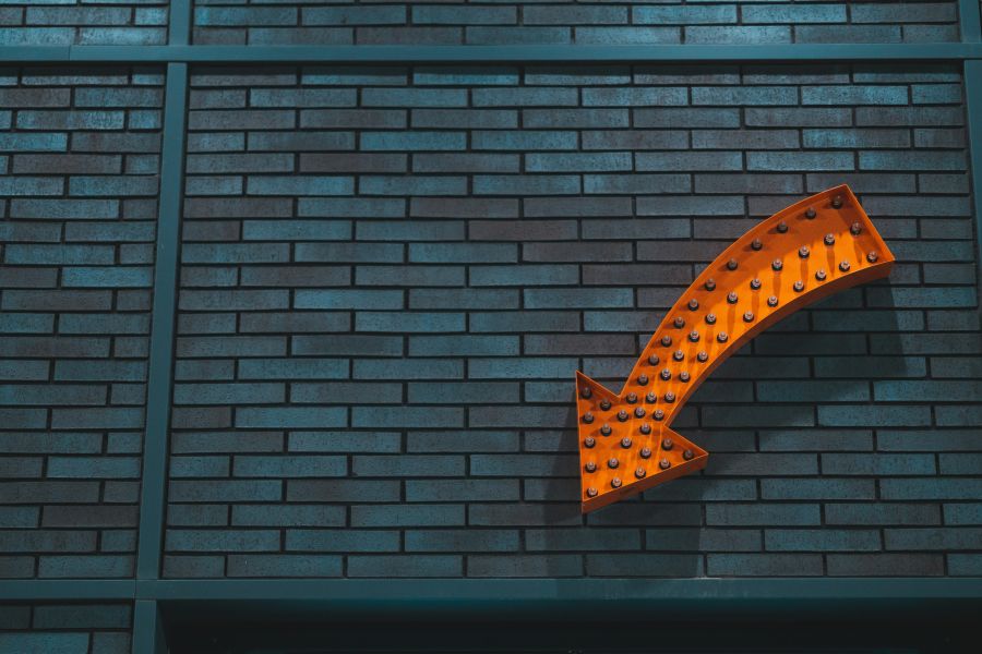 An orange arrow sign against a teal brick background inviting people to consider joining us at NeuroSpark Health.