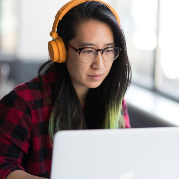 A woman with orange headphones focuses on her computer, representing neurodiversity at work.