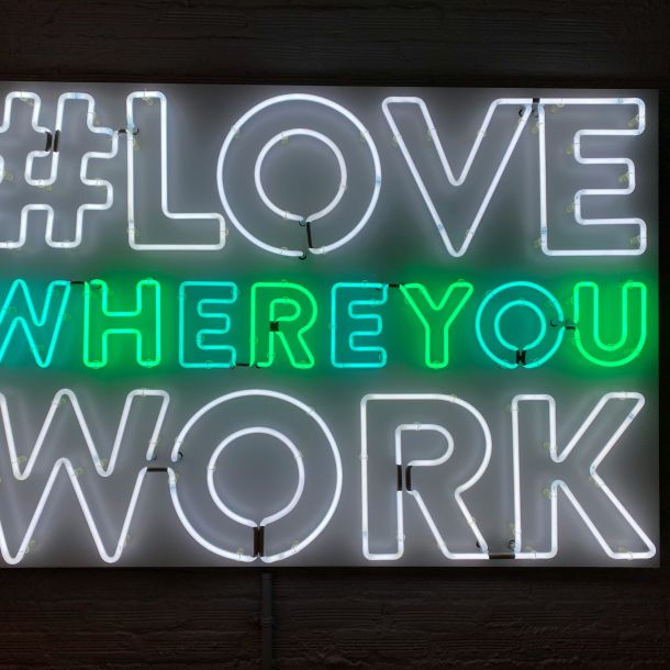 A white and green neon sign reads “#love where you work" representing NeuroSpark Health Careers.