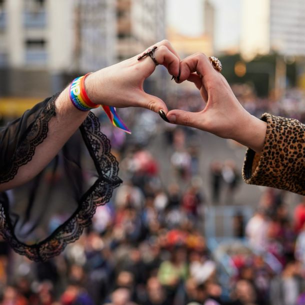 Two people at a Pride event form a heart shape with their hands, celebrating love and unity, symbolizing neuroqueer-resources.
