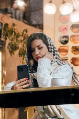 A woman wearing a scarf looks at her phone, considering her out-of-network benefits and insurance reimbursement details.
