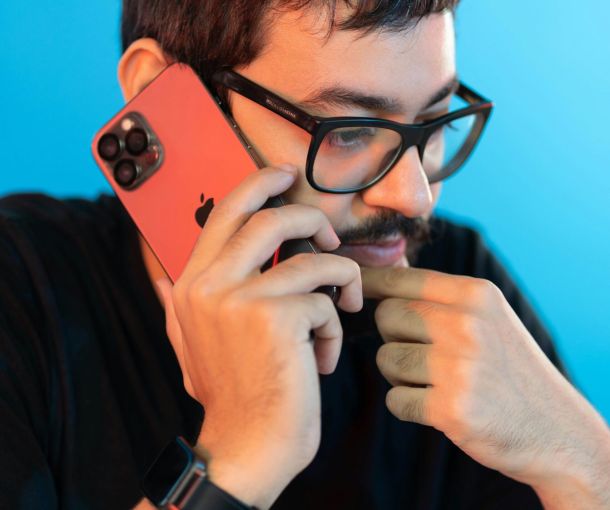 Man with black glasses and a black shirt talking on the phone with a pensive expression thinking about an adult ADHD assessment.