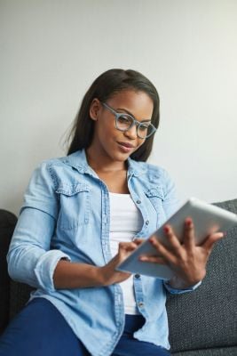 Woman sitting on a couch using an iPad while researching autism vs ADHD assessment options