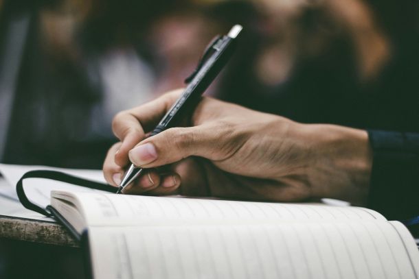A hand using a black pen to write in a notebook about adult-specific tools used in NeuroSpark Health's assessment process.