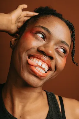 A joyful Black woman smiles with her head tilted and tongue out, embodying the vibrant spirit of Black autistic voices.