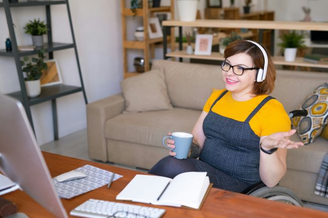 A woman in a yellow shirt holding a cup of coffee sits in front of her computer during an accommodations support session.
