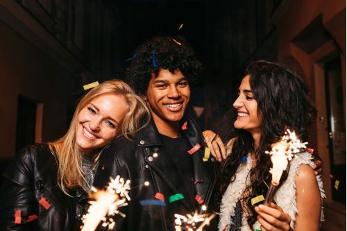 Three smiling people from the neurodivergent community hold lit sparklers.