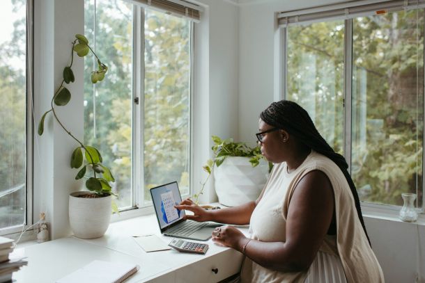 A woman works on a laptop in a bright, sunny office, completing a clinical interview for her adult AuDHD assessment.