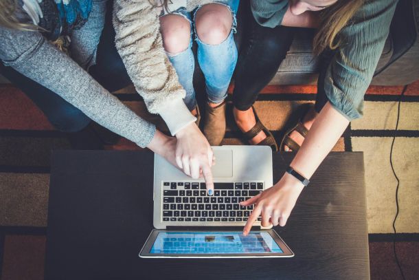 Several hands working on the same laptop represent the collective care of a neurodivergent community.