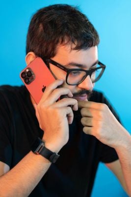 Man with black glasses and a black shirt talking on the phone with a pensive expression thinking about an adult ADHD assessment.