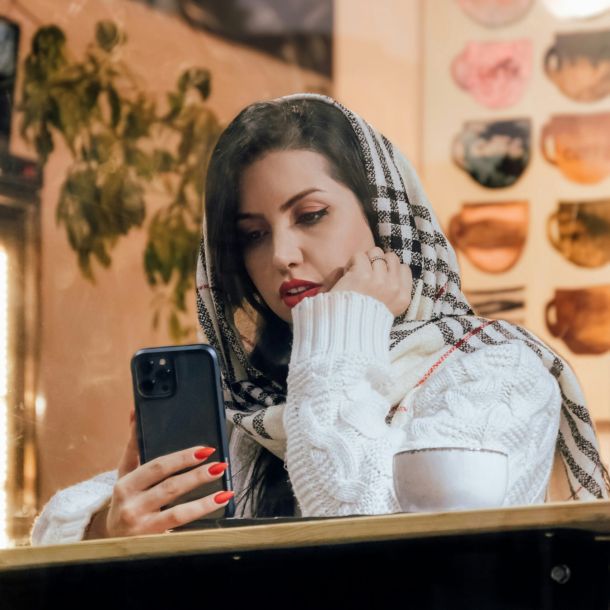 A woman wearing a scarf looks at her phone, considering her out-of-network benefits and insurance reimbursement details.