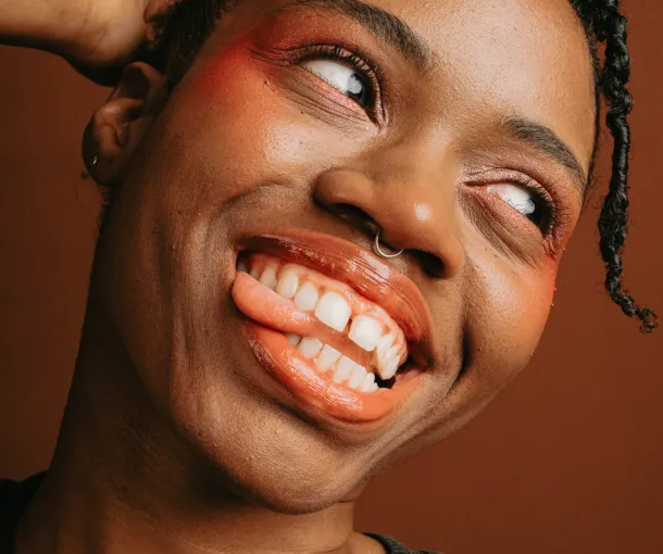 A joyful Black woman smiles with her head tilted and tongue out, embodying the vibrant spirit of Black autistic voices.