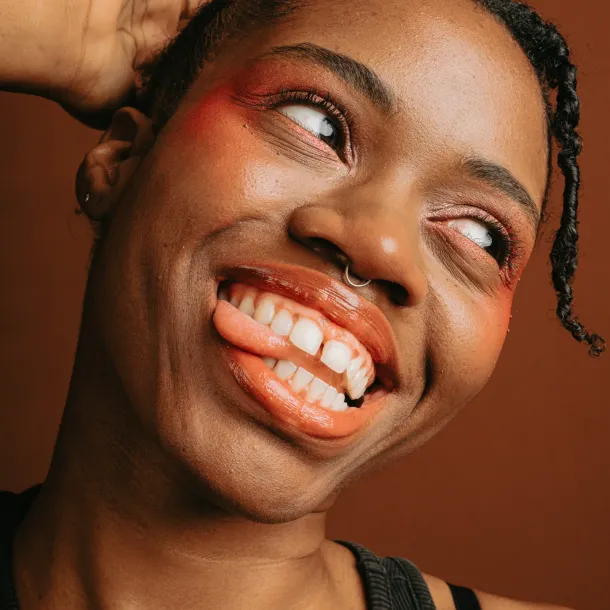A joyful Black woman smiles with her head tilted and tongue out, embodying the vibrant spirit of Black autistic voices.